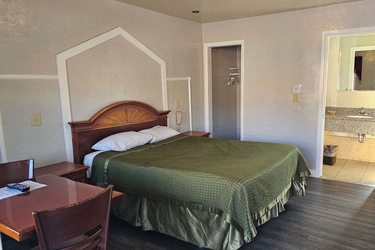 A hotel room with a bed, a desk with a chair, a telephone, and a bathroom visible through an open door.