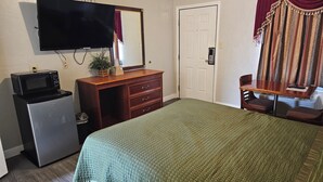 Ein Hotelzimmer mit Bett, Schreibtisch mit Stuhl, Kommode, Mikrowelle, Fernseher und Tür.