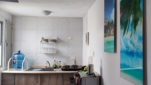 Una cucina con pareti in mattoni bianchi, un lavello, un distributore d'acqua di grandi dimensioni e un quadro raffigurante una spiaggia.