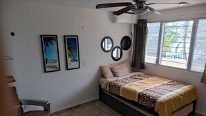 Una camera da letto con un letto, una ventola a soffitto, una finestra con tende e decorazioni a parete, tra cui quadri incorniciati.