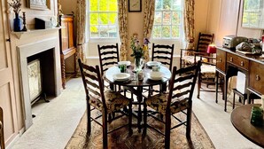 Une salle à manger avec une table ronde, des chaises, une cheminée et une fenêtre avec des rideaux.