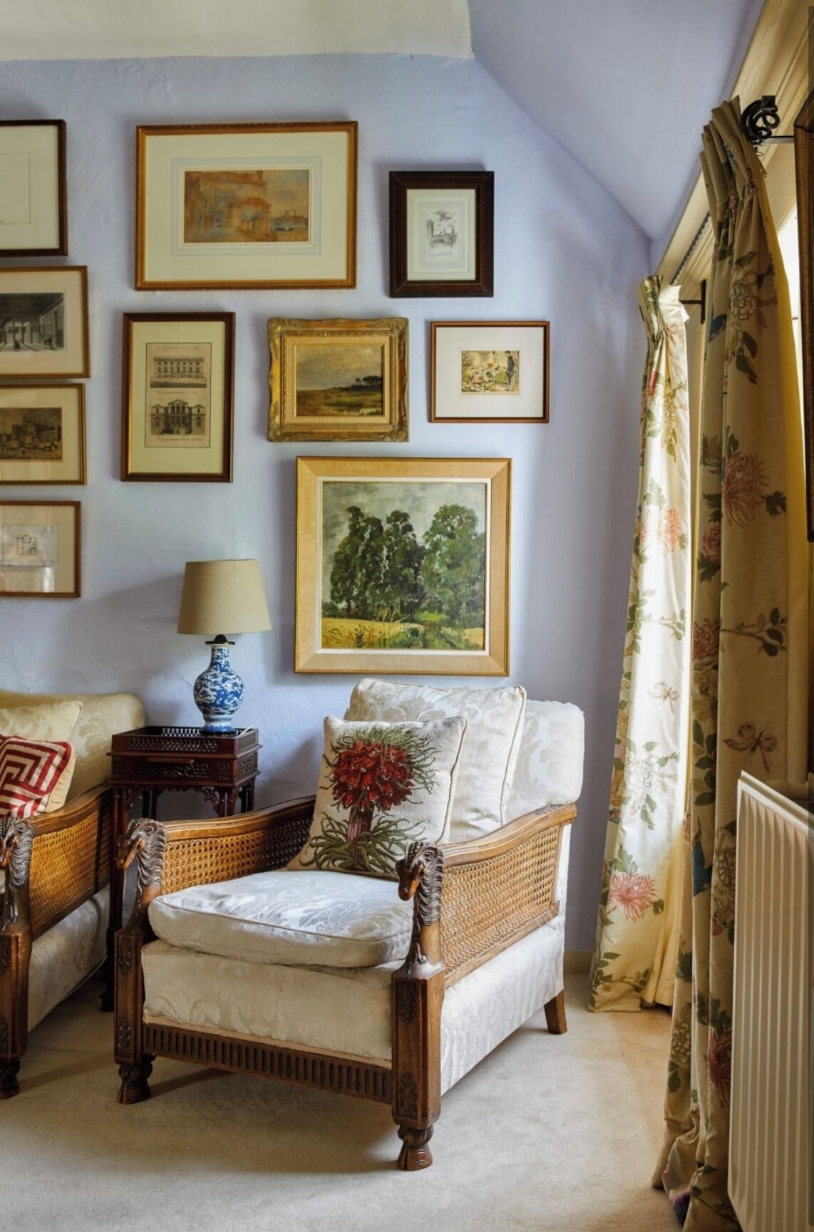 Une pièce comprenant un canapé traditionnel, une table d’appoint avec une lampe, et un mur décoré d’œuvres d’art encadrées.