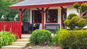 A house with a red porch, a wooden deck, and a garden with various plants and a bench. - 2 bedroom beautiful home in Toftlund (Toftlund)