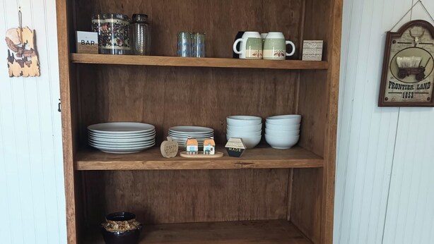 Una estantería de madera con frascos, tazas y platos.