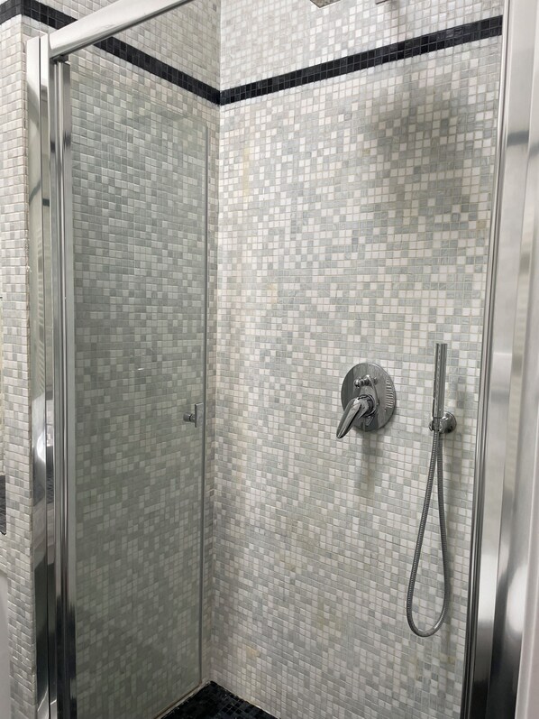 A glass-enclosed shower with a tiled wall and a handheld showerhead.