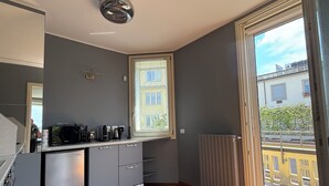 A modern kitchen with grey cabinets, a built-in microwave, and a window overlooking a balcony. - Duomo Attic Luxury Experience (Milano)