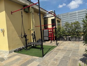 An outdoor gym with exercise equipment, a green artificial turf, and potted plants.