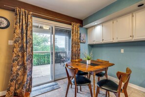 Een eetgedeelte met een houten tafel en stoelen, een schuifdeur van glas naar een terras, en witte kasten erboven.