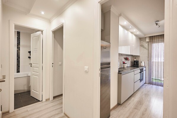 A modern kitchen with a built-in oven, microwave, and sink. There is a small island with a sink and a potted plant. The kitchen has a light wood floor and white walls.