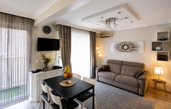 A modern living room with a sofa, a dining table with chairs, a TV mounted on the wall, and a decorative wall piece.