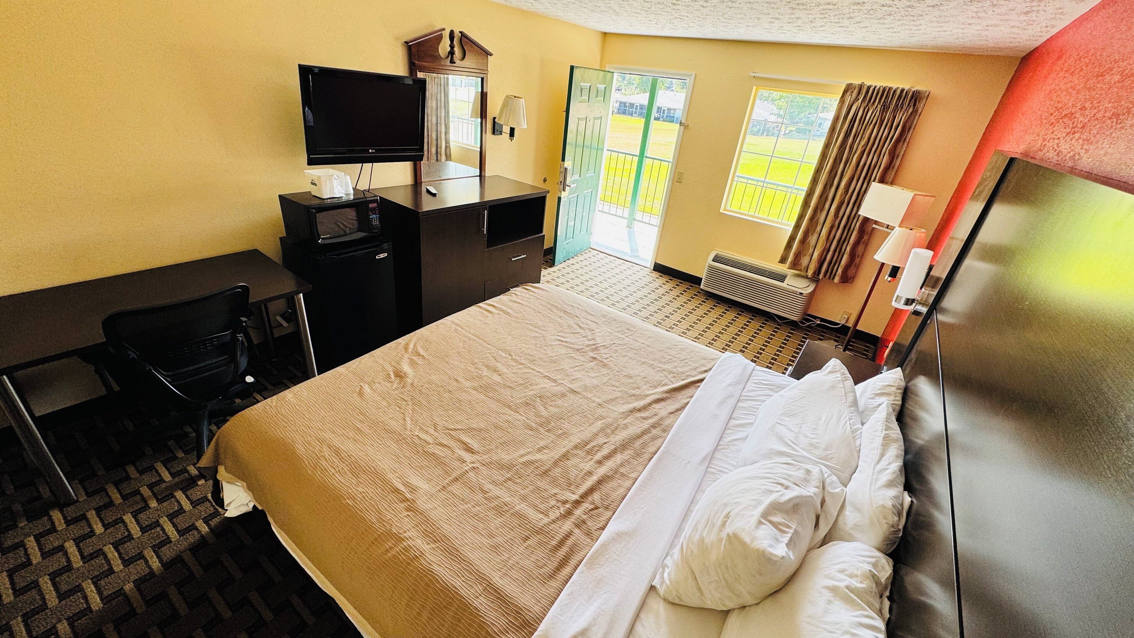 Habitación de hotel con cama, escritorio con ordenador, televisor y ventana con cortinas.