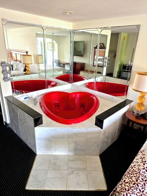 A bathroom with a large red bathtub, a mirror, and a sink. - Garden Inn & Suites (Pine Mountain)