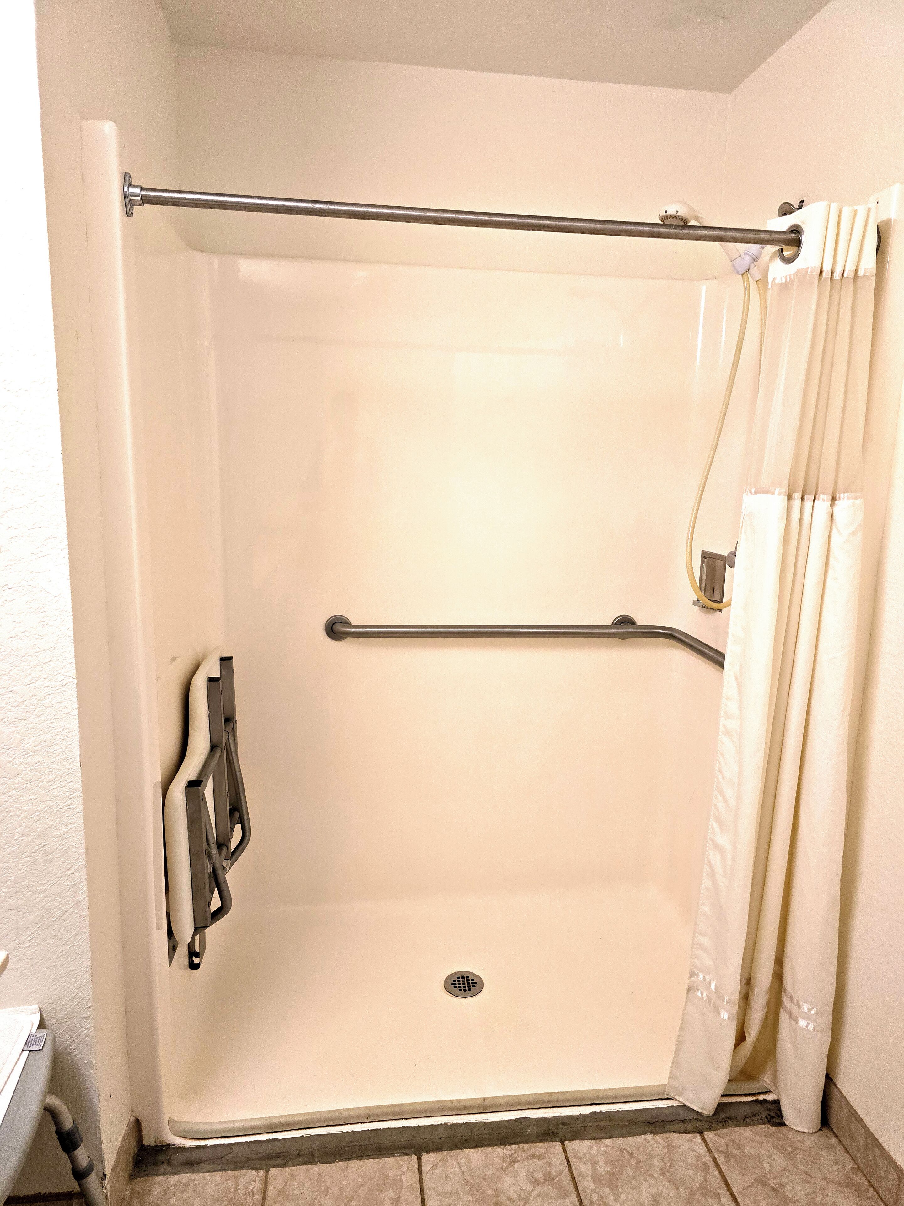 A shower stall with a grab bar, a handheld showerhead, and a curtain.