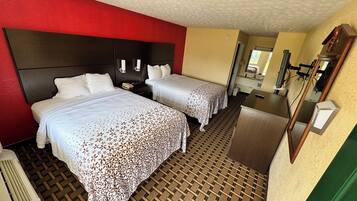 Una habitación de hotel con dos camas, un espejo grande, un escritorio y una pared de acento roja.
