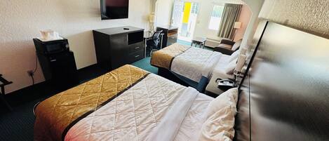 A hotel room with two beds, a desk, a TV, and a bathroom.
