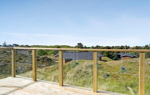 Een houten terras met glazen hekwerk met uitzicht op een woongebied met huizen en een glooiend landschap.
