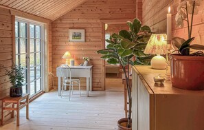 Cozy room with a dining area, potted plant, and framed picture, set against a warm wooden ceiling and floor.
