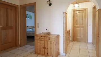 Un corridoio con porte in legno, pavimento piastrellato e un piccolo mobile contenitore con cassetti.