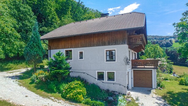 A two-story house with a sloped roof, a wooden balcony, and a garage.