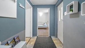 A narrow hallway with a bed at the end, a welcome sign, and a small shelf with a plant.
