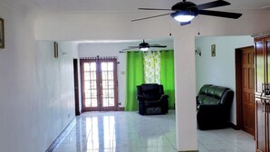 Un amplio salón con ventilador de techo, un sofá y una cortina verde.