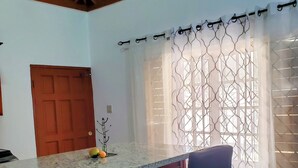 Una cocina con encimera de granito, armarios de madera, un taburete negro, una puerta de madera y una ventana con cortinas estampadas.