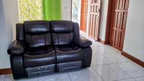 Un sofá de cuero negro en un pasillo con una cortina verde, puertas de madera y suelo de baldosas.