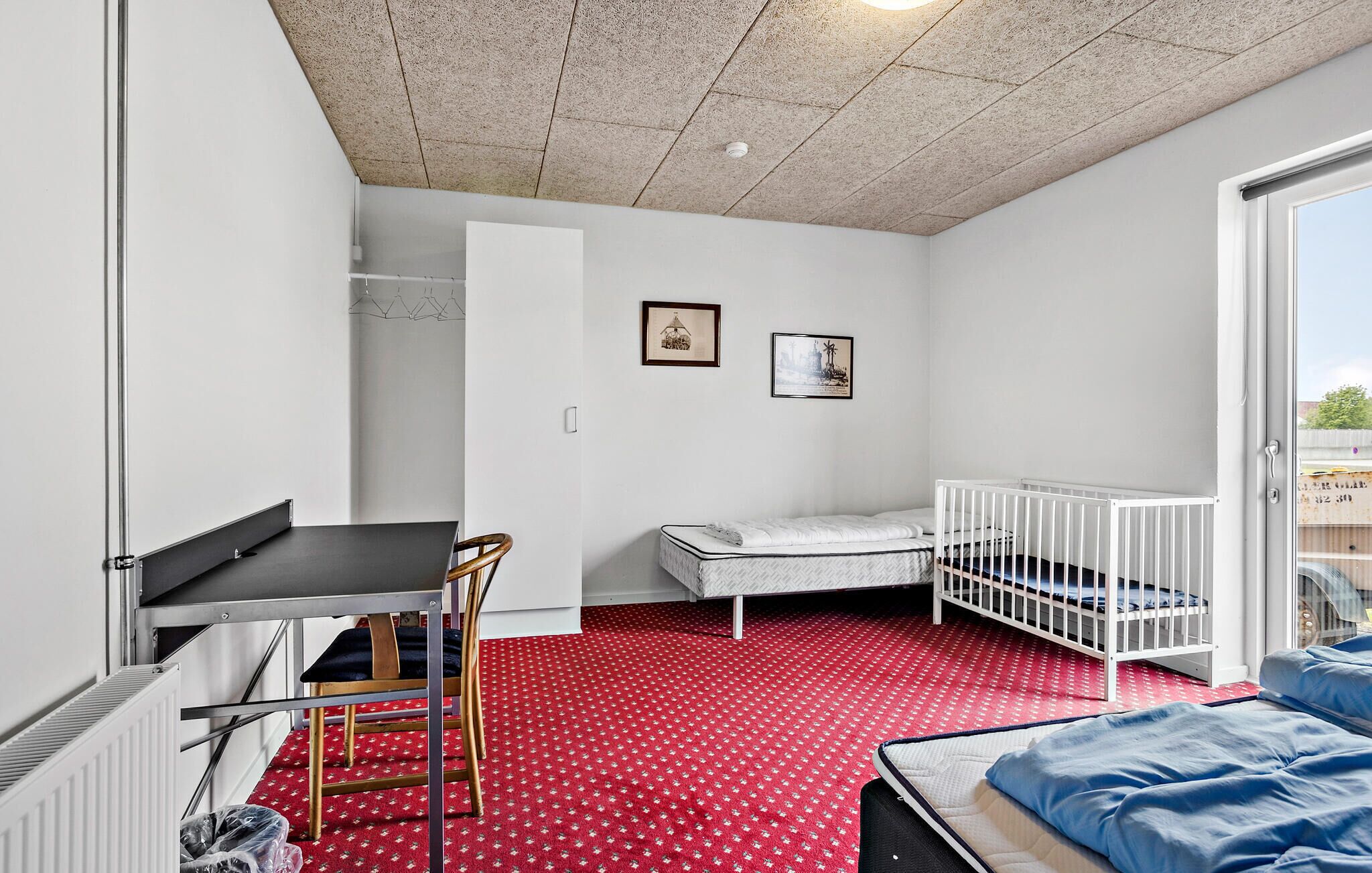 Una habitación compacta con cama, cuna, escritorio y silla, y un radiador.