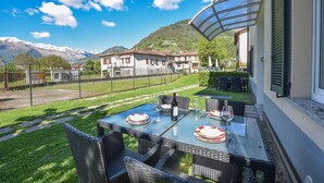 Une table en verre installée à l’extérieur, avec des chaises, offrant une vue sur la montagne et une maison en arrière-plan.