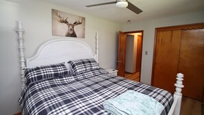 A neatly made bed with a checkered bedspread, a white headboard, and a ceiling fan. - The Maine House in State College - 2 miles to PSU via walking path or car! (State College)