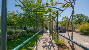 A covered pathway with a metal frame, surrounded by greenery and a parked car. - Beautiful home in Zavojane (Zavojane)