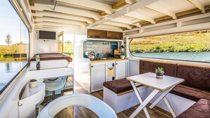 A compact, well-lit interior with a kitchenette, seating area, and a window overlooking a water body. - Lovely ship in Ophoven with lake view (Ophoven)