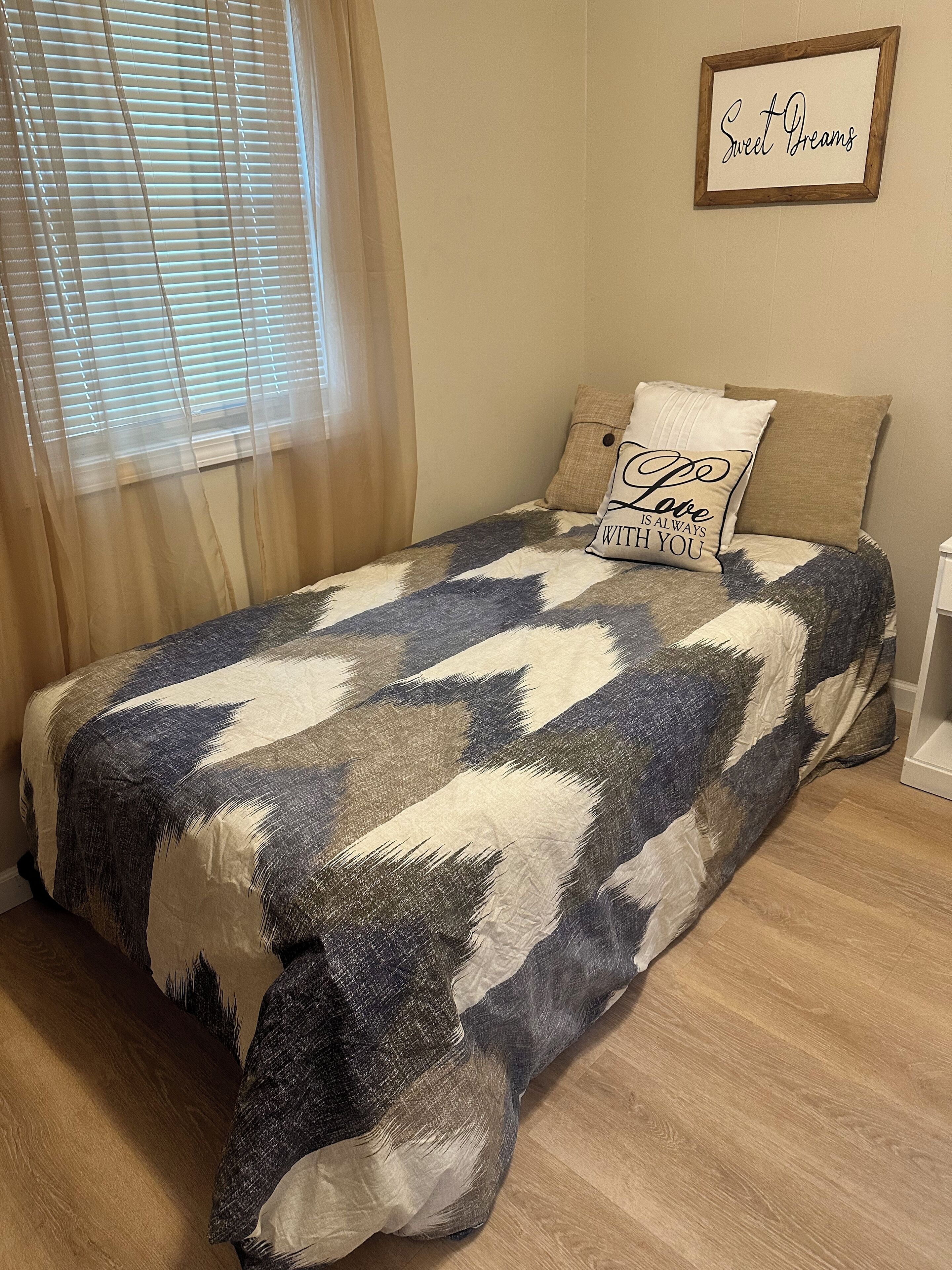 Una camera da letto con un letto, una finestra con persiane, un cartello appeso al muro e un comodino.