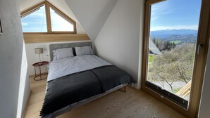 Un dormitorio con techo inclinado, un ventanal grande y vistas a un paisaje montañoso.