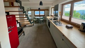 Una cocina moderna con un refrigerador rojo, una escalera de madera y vistas a las montañas a través de amplios ventanales.