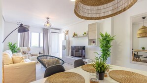 A modern living room with a sofa, chairs, a TV, and a dining area with placemats. - Stunning apartment in El Campello with WiFi (El Campello)