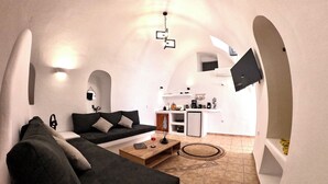 A compact living space with a sofa, coffee table, and a kitchen area with a TV. - Wine Cellar House | Exclusive retreat that redefines luxury living in Santorini (Thira)