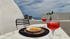 A table with a plate of food and a glass of red wine, set against a white wall with a view of the sky. - Wine Cellar House | Exclusive retreat that redefines luxury living in Santorini (Thira)