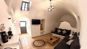 A modern living room with a sofa, coffee table, and a TV mounted on the wall. - Wine Cellar House | Exclusive retreat that redefines luxury living in Santorini (Thira)