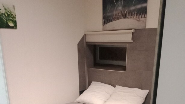 Une petite chambre avec un lit simple, une tête de lit, une table de chevet et une étagère fixée au mur au-dessus du lit.