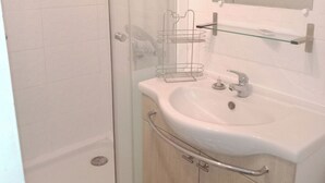 Une salle de bain avec une douche à parois de verre, un lavabo blanc avec un miroir au-dessus et un meuble en bois en dessous.