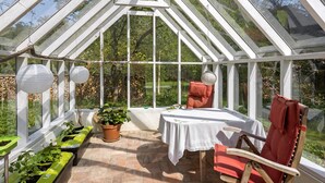 A greenhouse with a table and chairs, potted plants, and a stone wall.