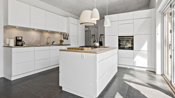 A modern kitchen with white cabinetry, a central island, pendant lighting, and a built-in oven.