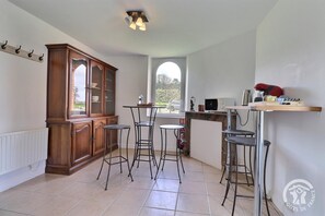 Une cuisine avec un meuble en bois, trois tabourets, une petite table et un micro-ondes posé sur une étagère.