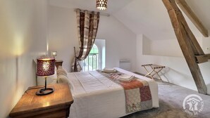Une chambre à coucher avec un lit, une table de chevet, une lampe, une chaise en bois et une fenêtre avec des rideaux.