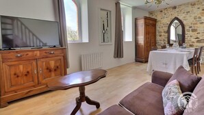 Un salon avec un meuble en bois, un téléviseur, une table à manger dressée pour deux personnes et un mur en pierre.