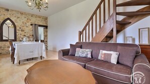 Un salon chaleureux avec un escalier en bois, un coin repas avec une table mise pour deux personnes et un mur en pierre.