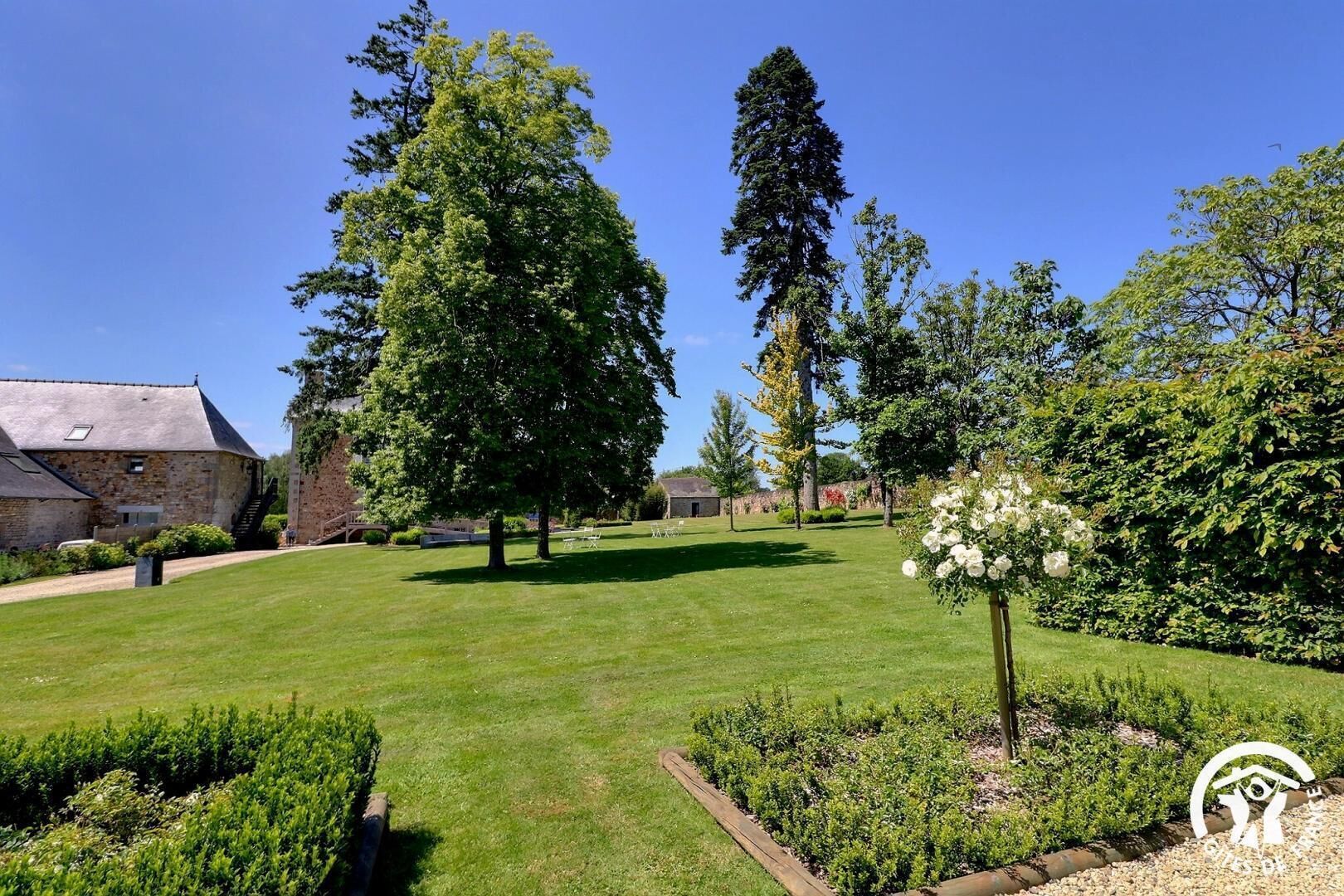 Un jardín bien cuidado con diferentes árboles, césped y parterres de flores.