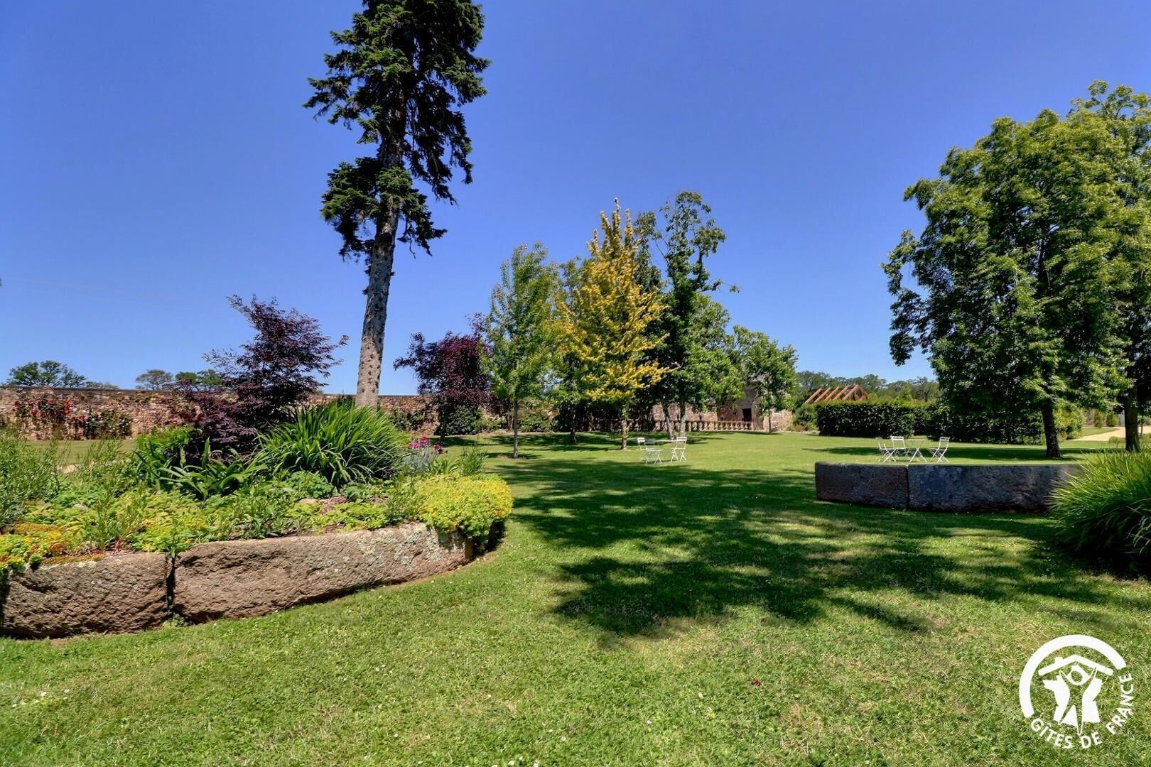 A well-maintained garden with a variety of trees and shrubs, a grassy lawn, and a stone wall.