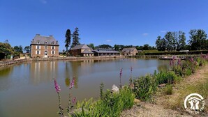 Un grand bâtiment en pierre, avec un étang devant, entouré de verdure et d’arbres.